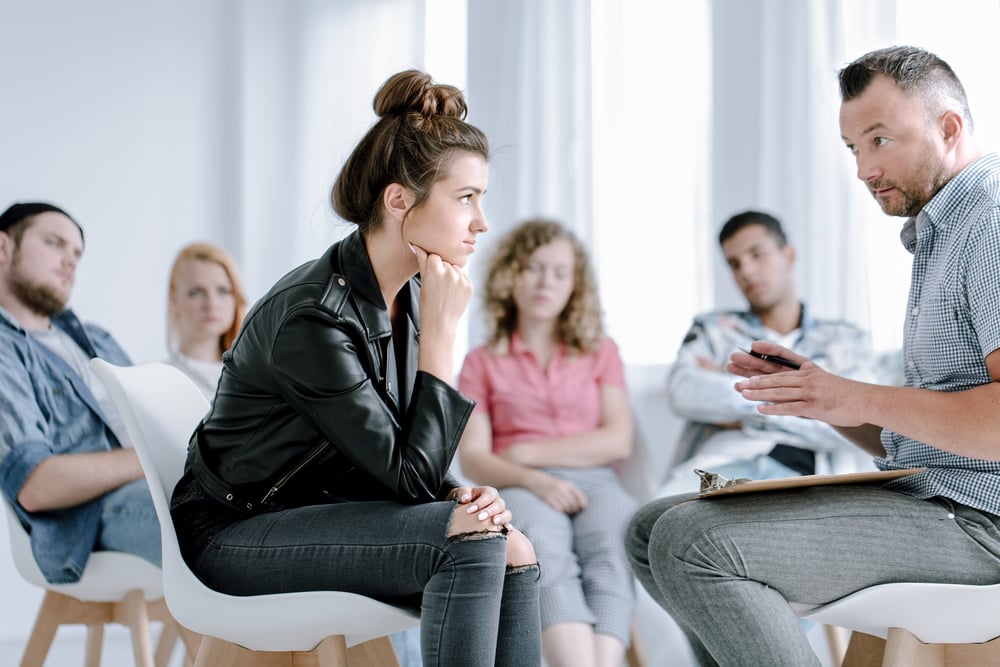 Rebellious young girl listening to her counselor during group therapy for PTSD