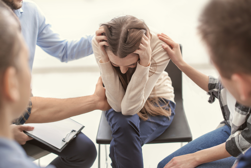 woman with sexual trauma undergoing group therapy while people are consoling her