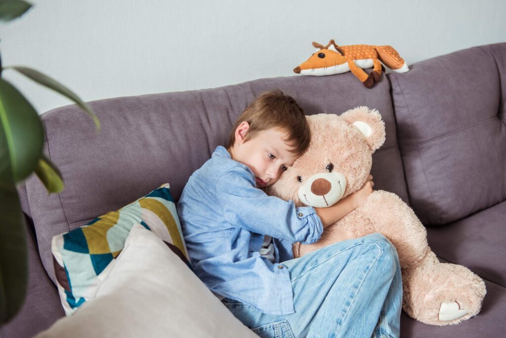 a young boy sits on the sofa, clutching a teddy bear—a poignant symptopm of childhood trauma