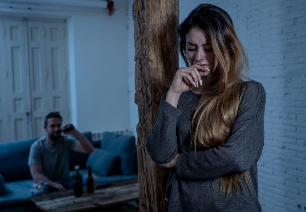 woman showing signs of trauma and a possible abuser sitting behind her