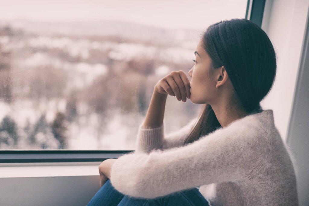 depressed woman looking out the window alone