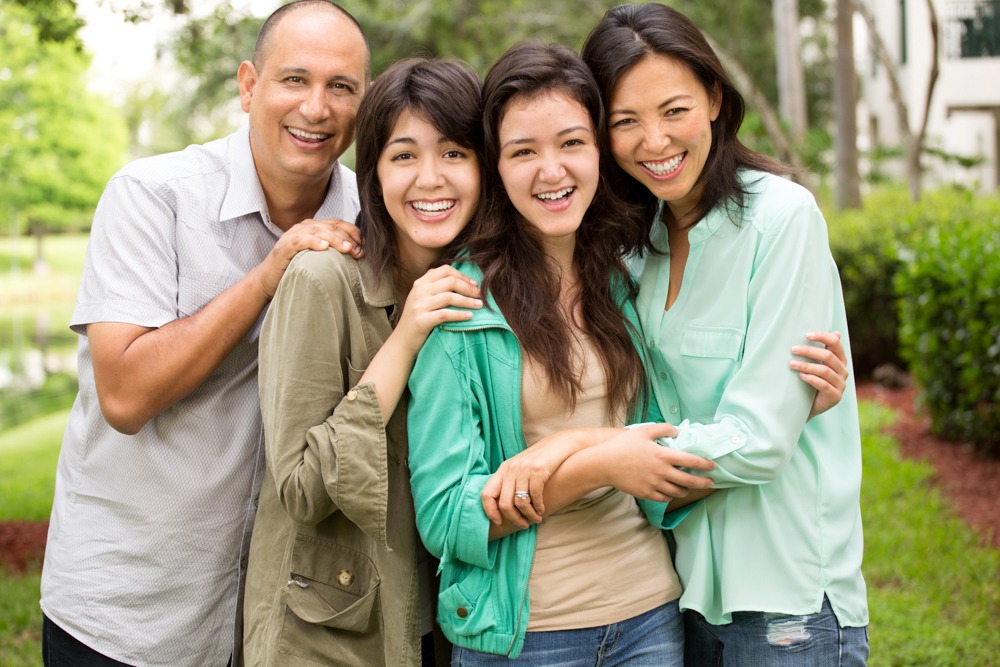 A family of four smiles together for a photo, showcasing their joyful bond and togetherness in a warm setting