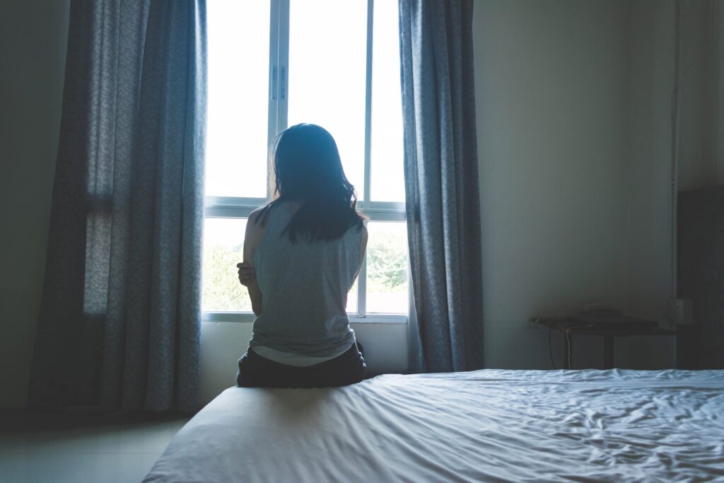 woman sitting on bed in room with light from window showing signs of abused