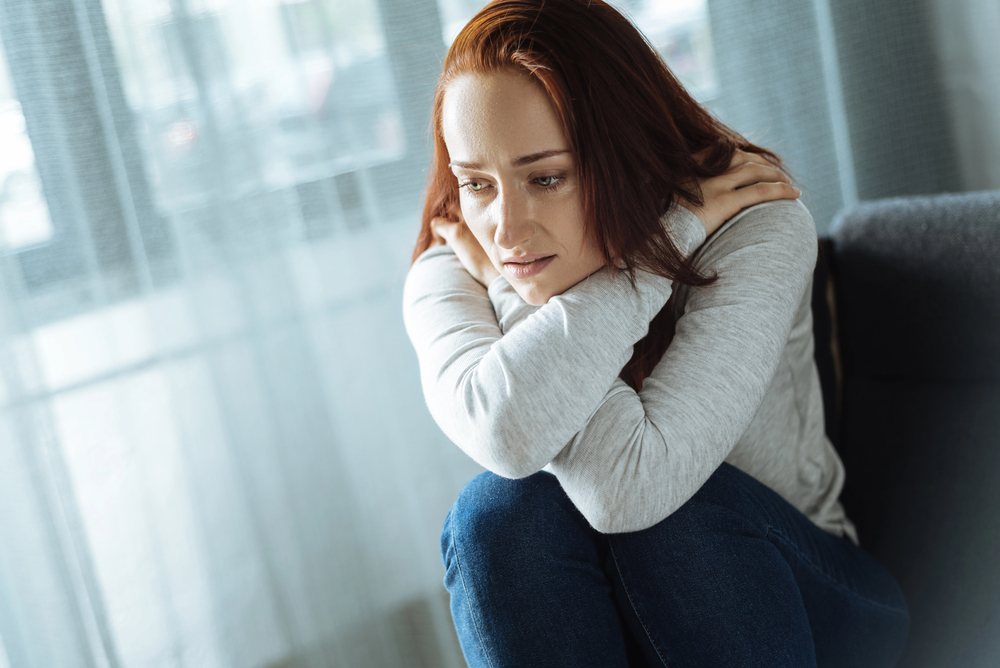 A woman sitting alone, embracing herself while experiencing depression