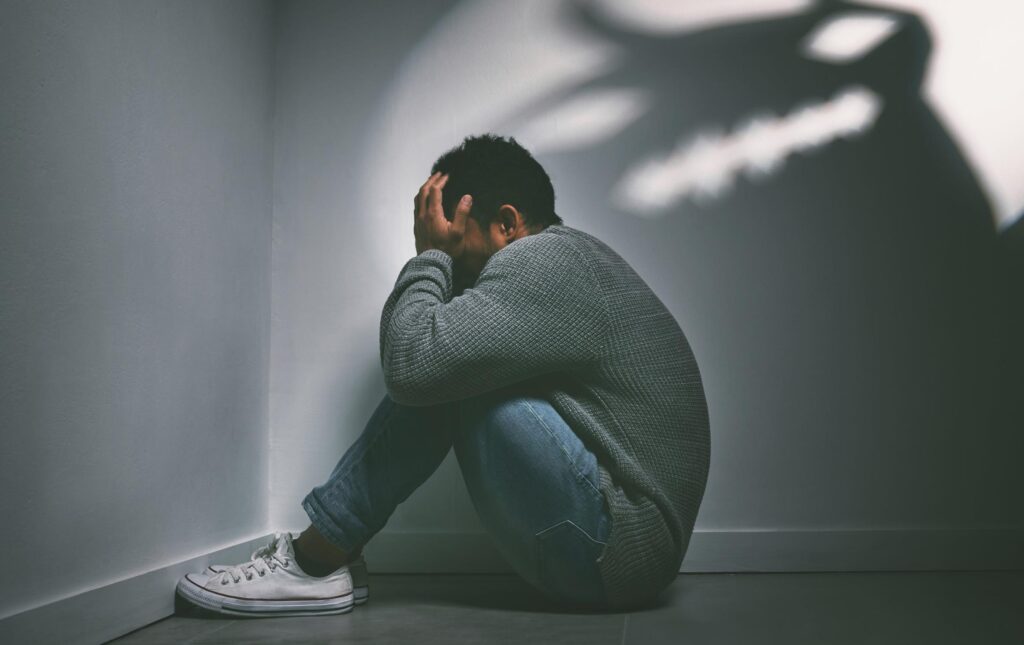 shot of a young man sitting in the corner of a dark room with trauma