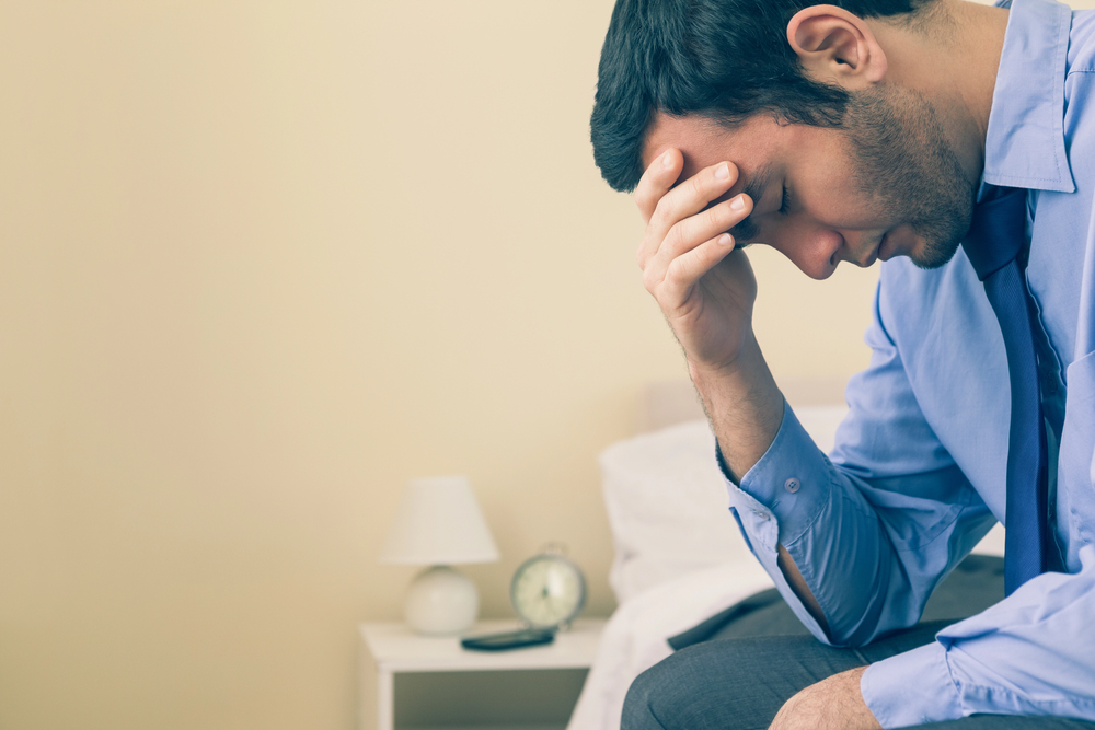 A man sitting on a bed, holding his head while coping with depression