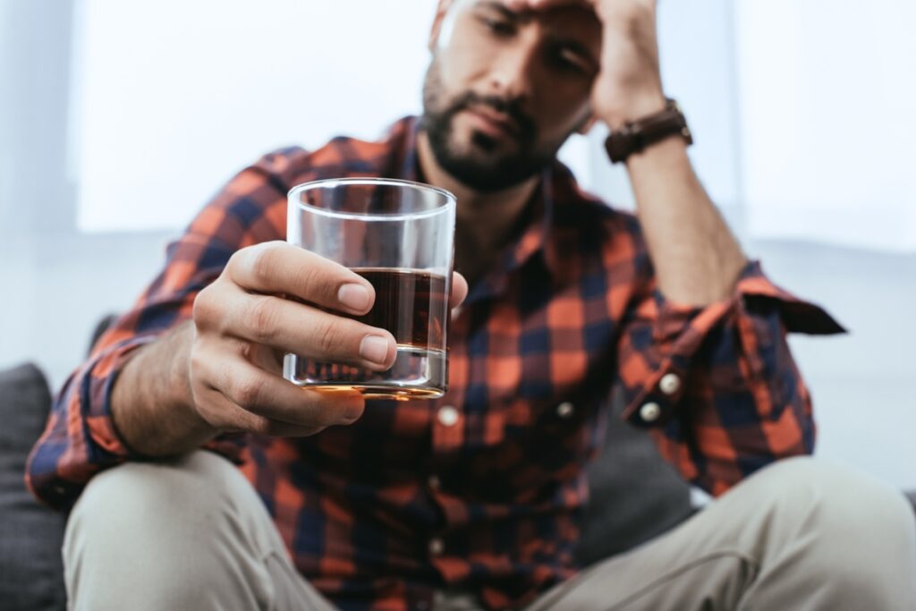 close-up shot of depressed young man with glass of whiskey