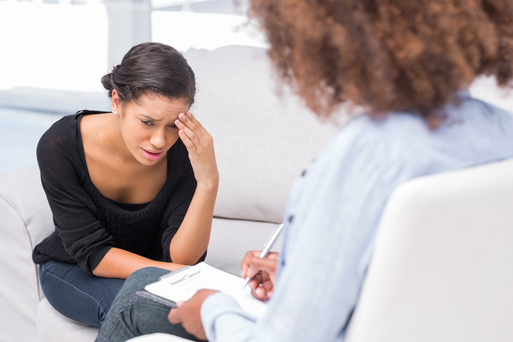 young woman looking depressed holding her head while talking to a therapist.