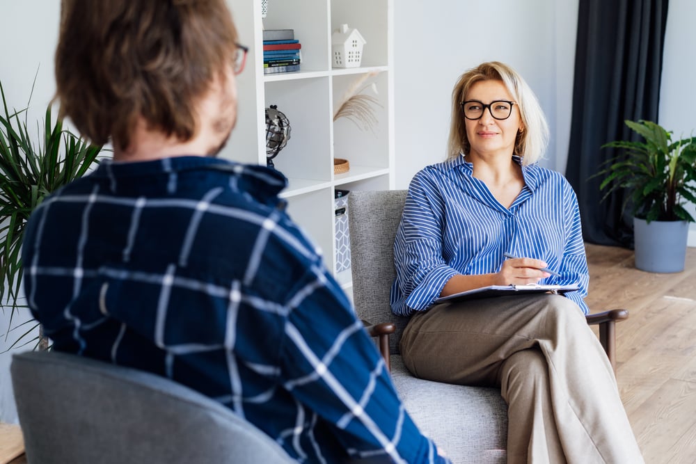 Female psychologist having session with male patient at mental health clinic, Taking Notes During Appointment