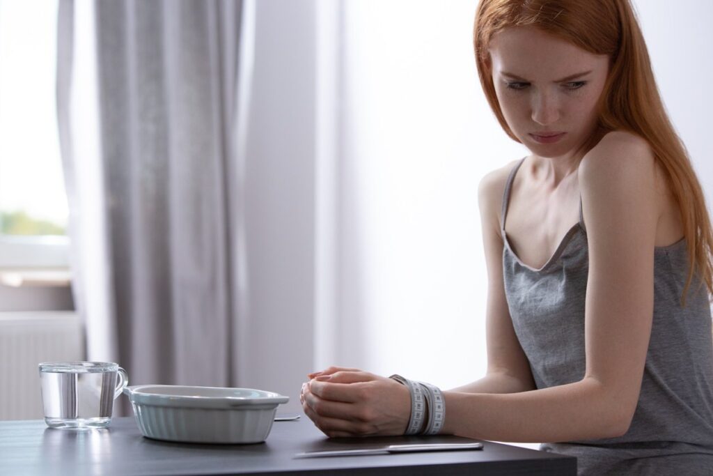 Young girl with eating disorder sitting with her hands tied with measuring tape