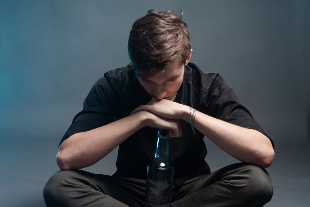 The brooding man leans on an empty bottle of alcohol on a grey background