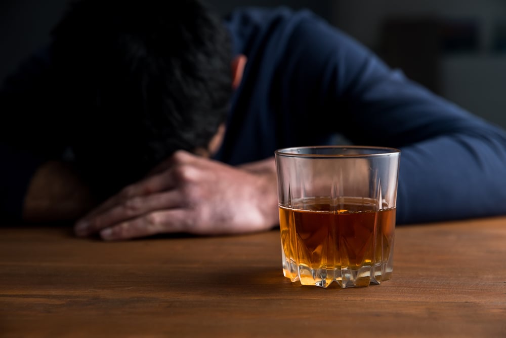 sad man with glass of whiskey on desk