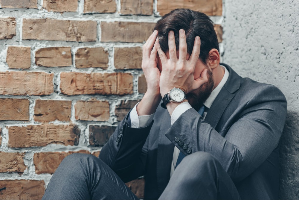 a depressed man in a coat sitting on the brick floor 