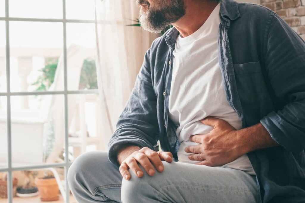 Man suffering with severe stomach pain sitting at home. Hand of mature guy holding abdomen suffering from gastritis due to alcohol